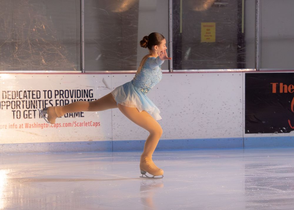 Young female figure skater in light blue dress performing a graceful spin on ice. Hagerstown, Maryland.