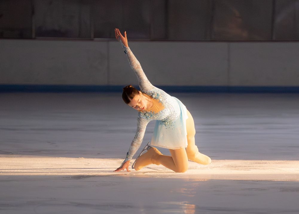 Figure skater in white costume performing a graceful floor pose on ice rink. Hagerstown, Maryland.