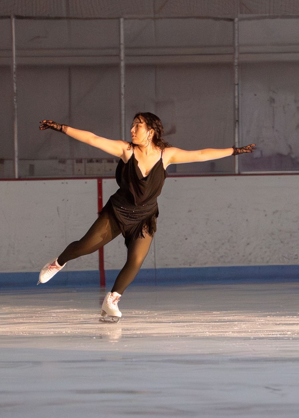 Female figure skater in black dress performing an elegant arabesque on ice rink. Hagerstown, Maryland.