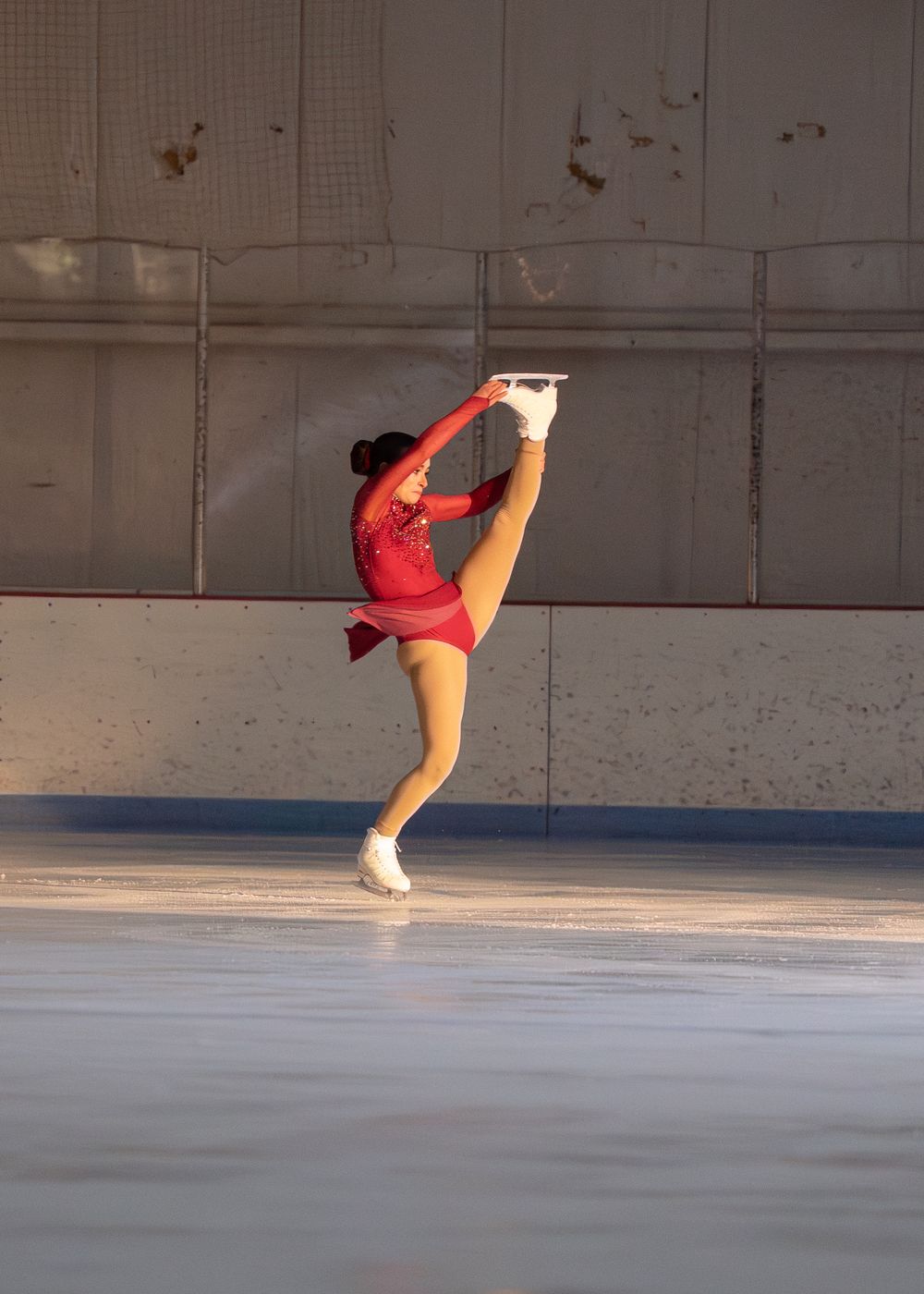 Female figure skater in red dress performing a high leg extension on ice. Hagerstown, Maryland.