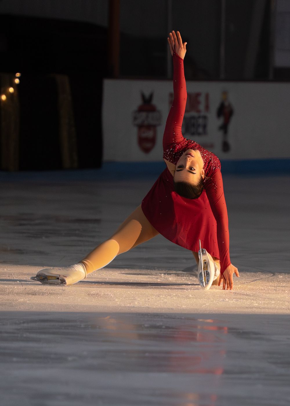 Figure skater in red costume performing a dramatic layback spin on ice rink. Hagerstown, Maryland.