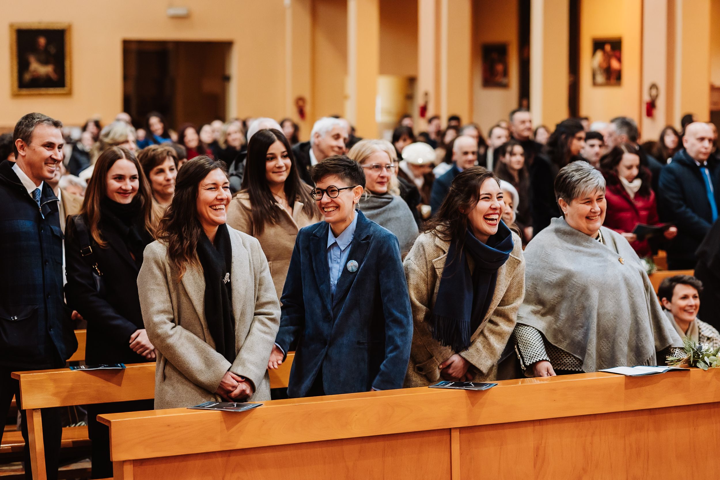 Wedding guests smiling and laughing in church pews during a ceremony celebration.