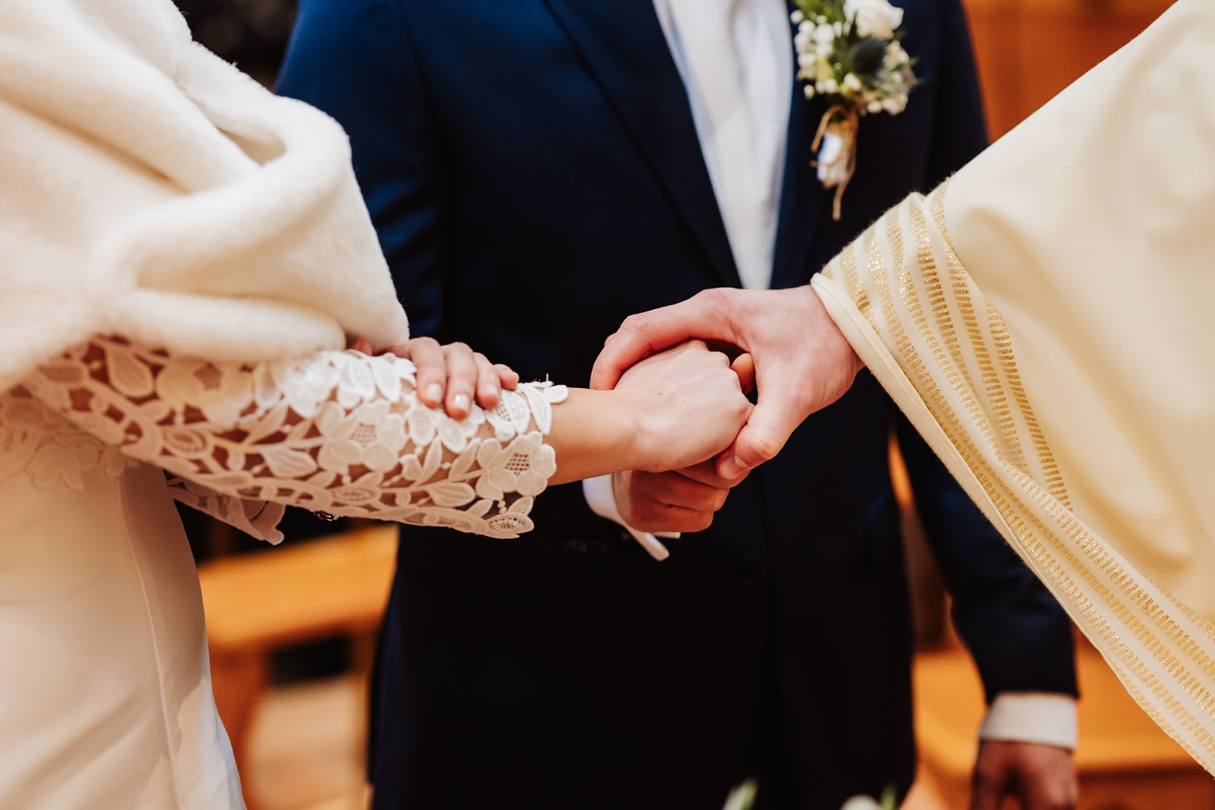 Bride and groom holding hands during wedding ceremony with officiant, bride wearing lace dress.