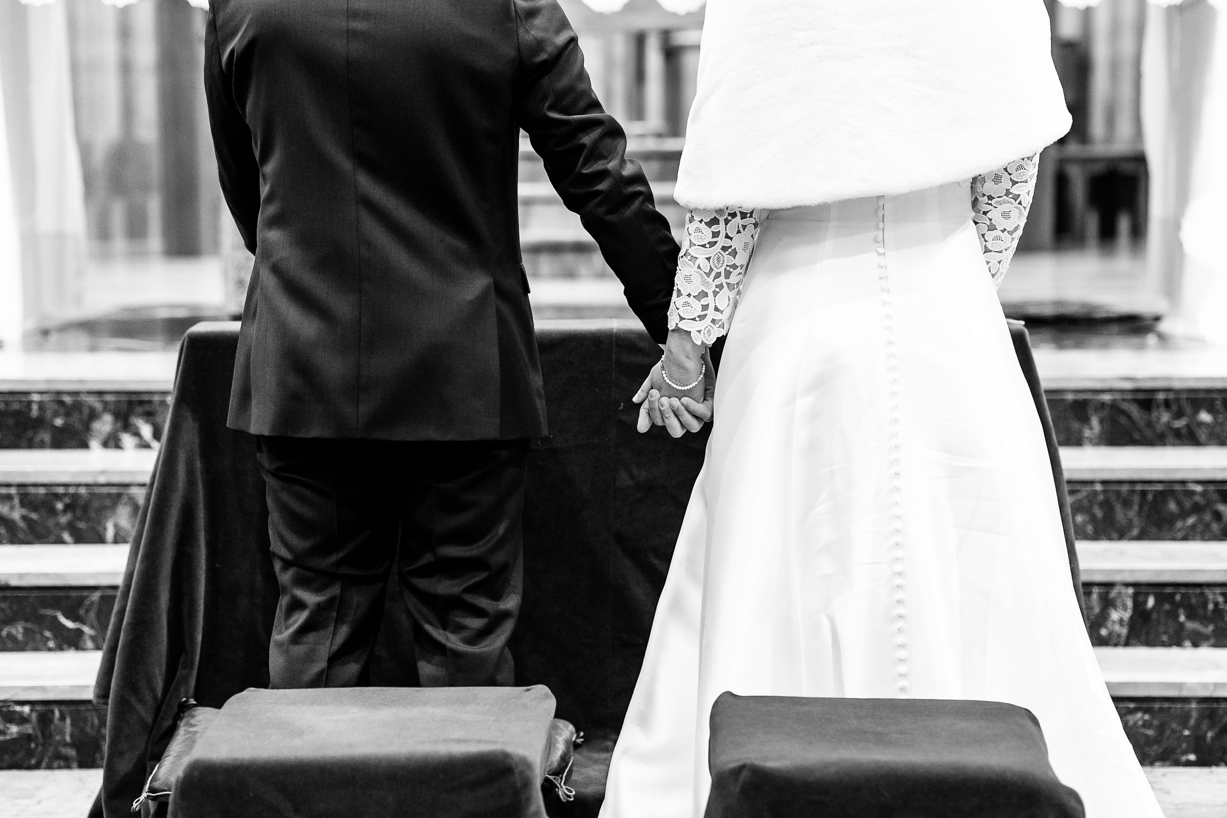 Bride and groom holding hands from behind at church altar in black and white wedding photo.