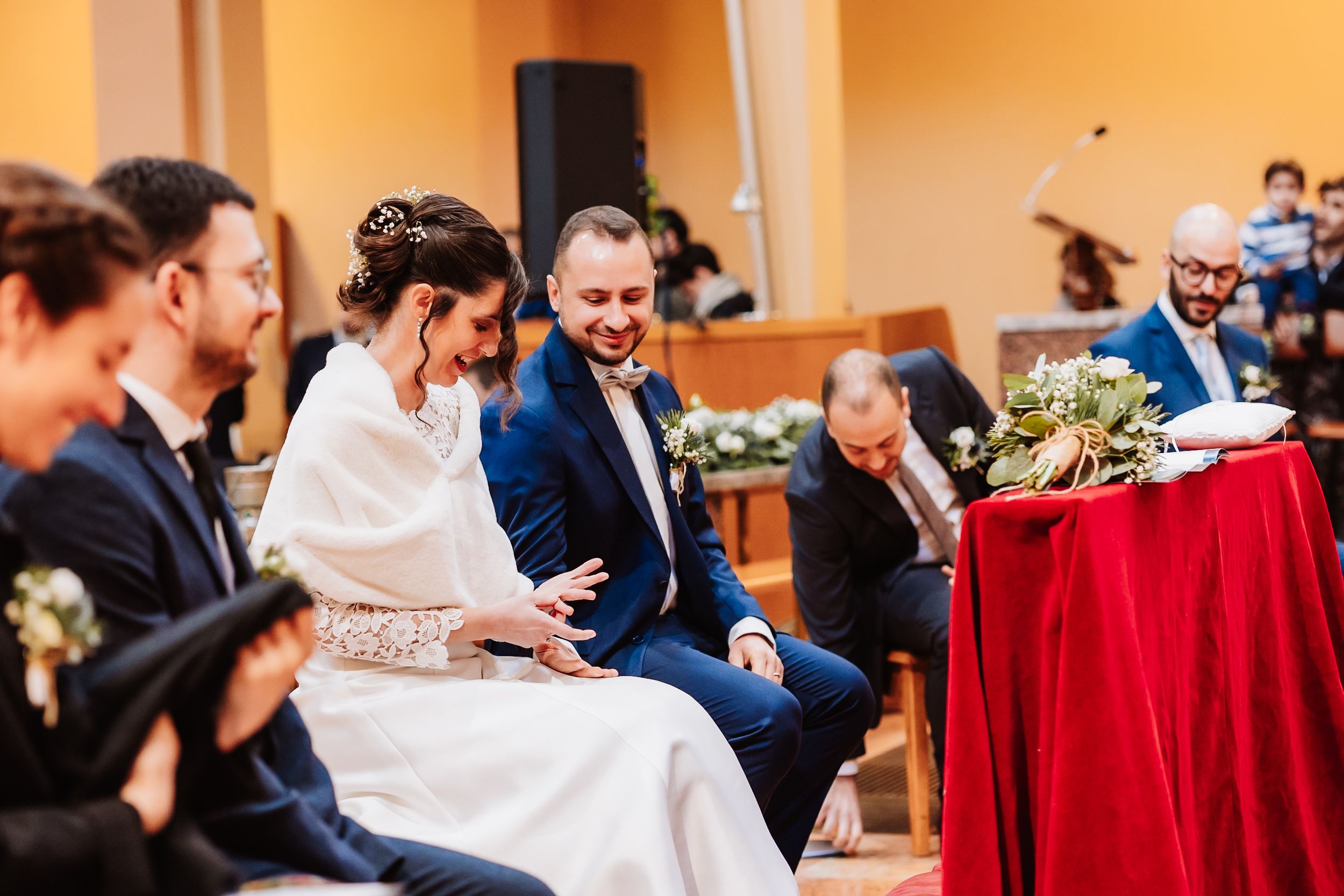 Bride and groom share a joyful moment seated at their wedding ceremony, surrounded by guests in elegant attire.