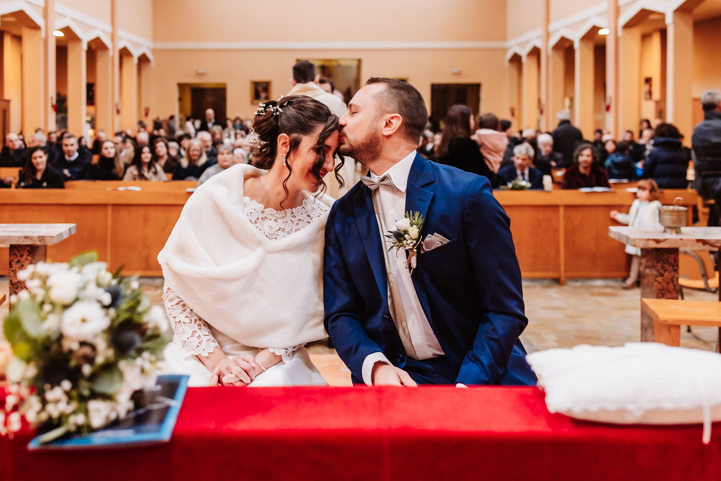 Bride and groom share a kiss at the altar during their church wedding ceremony, surrounded by guests in pews.