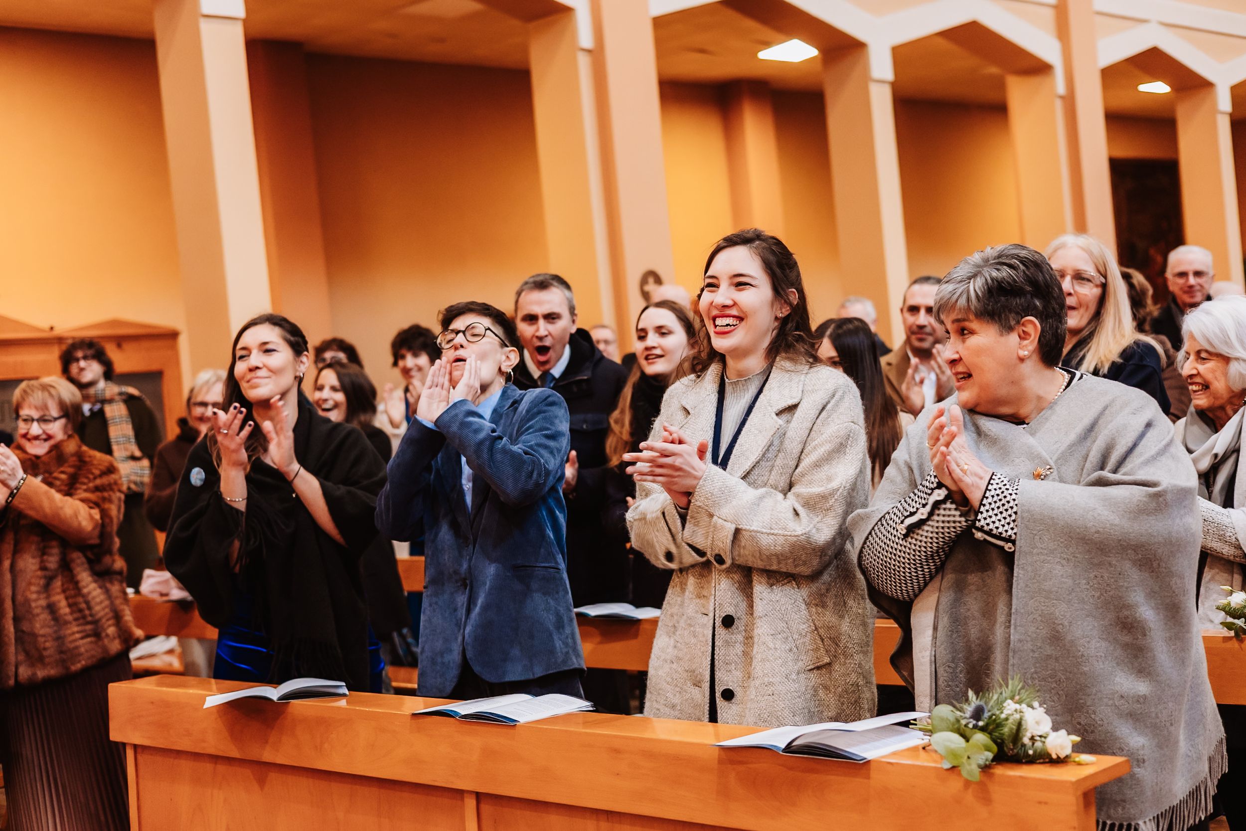 Audience members clapping and smiling during an indoor event in a bright hall.