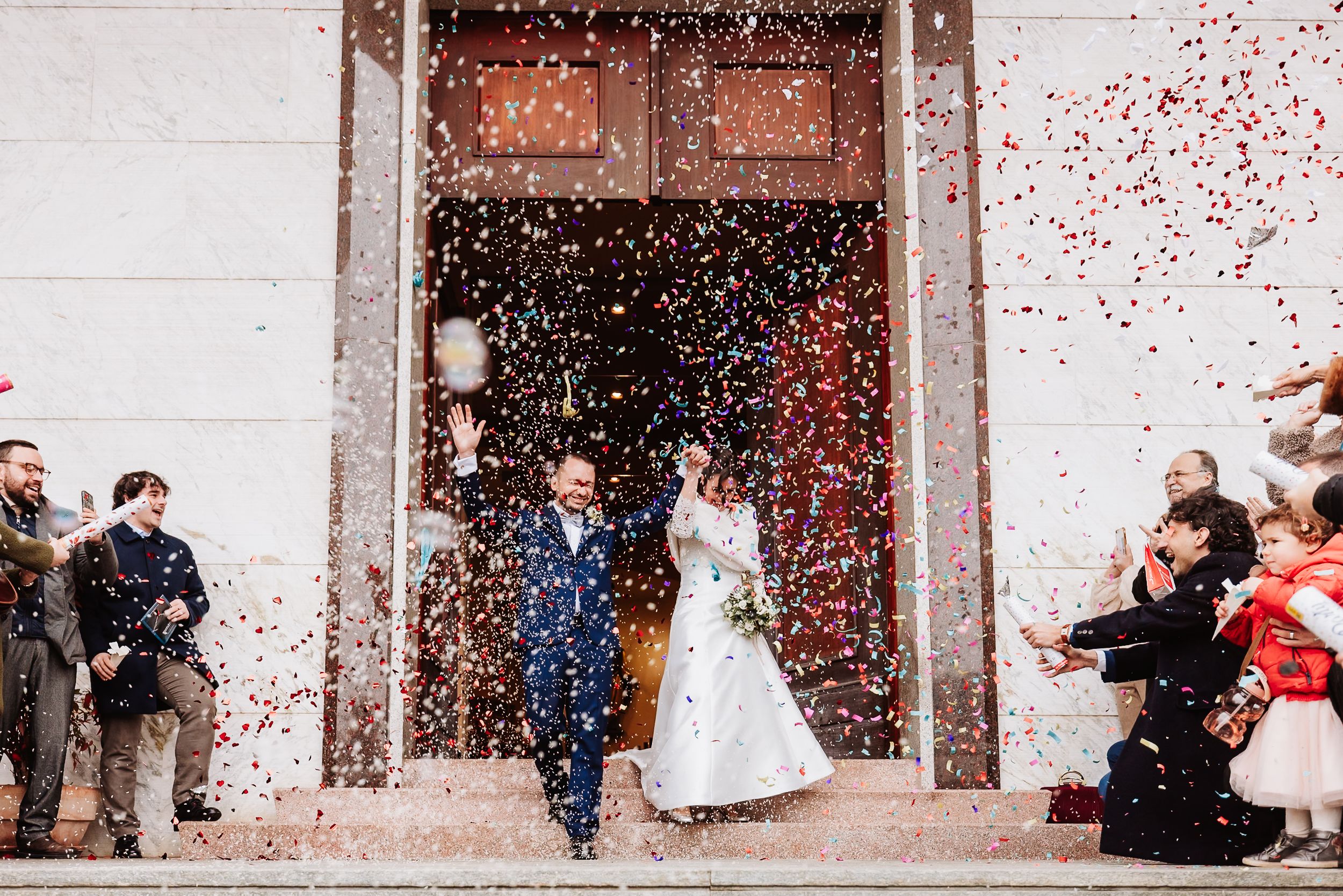 Newlyweds exit church doors as guests shower them with colorful confetti during a joyful wedding celebration.