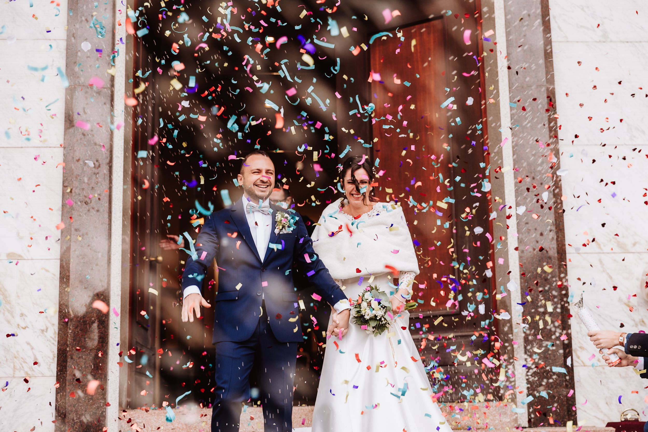 Bride and groom celebrate outside with colorful confetti falling around them on their wedding day.