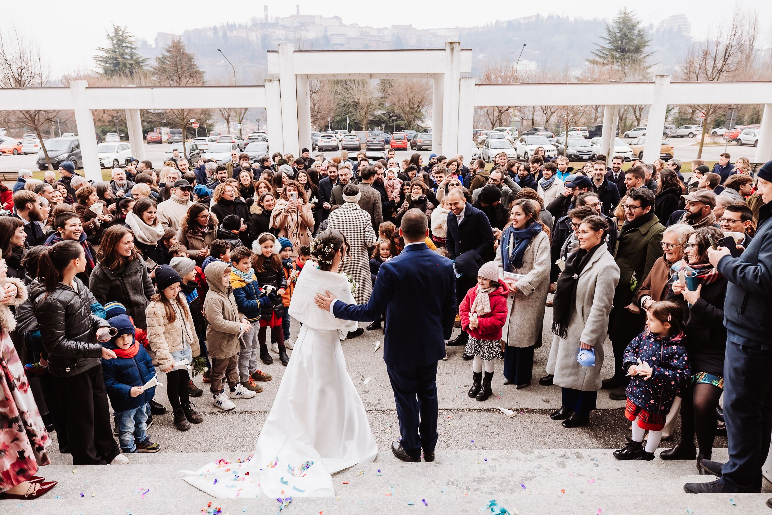 Bride and groom walk down the aisle surrounded by wedding guests outdoors in winter setting.
