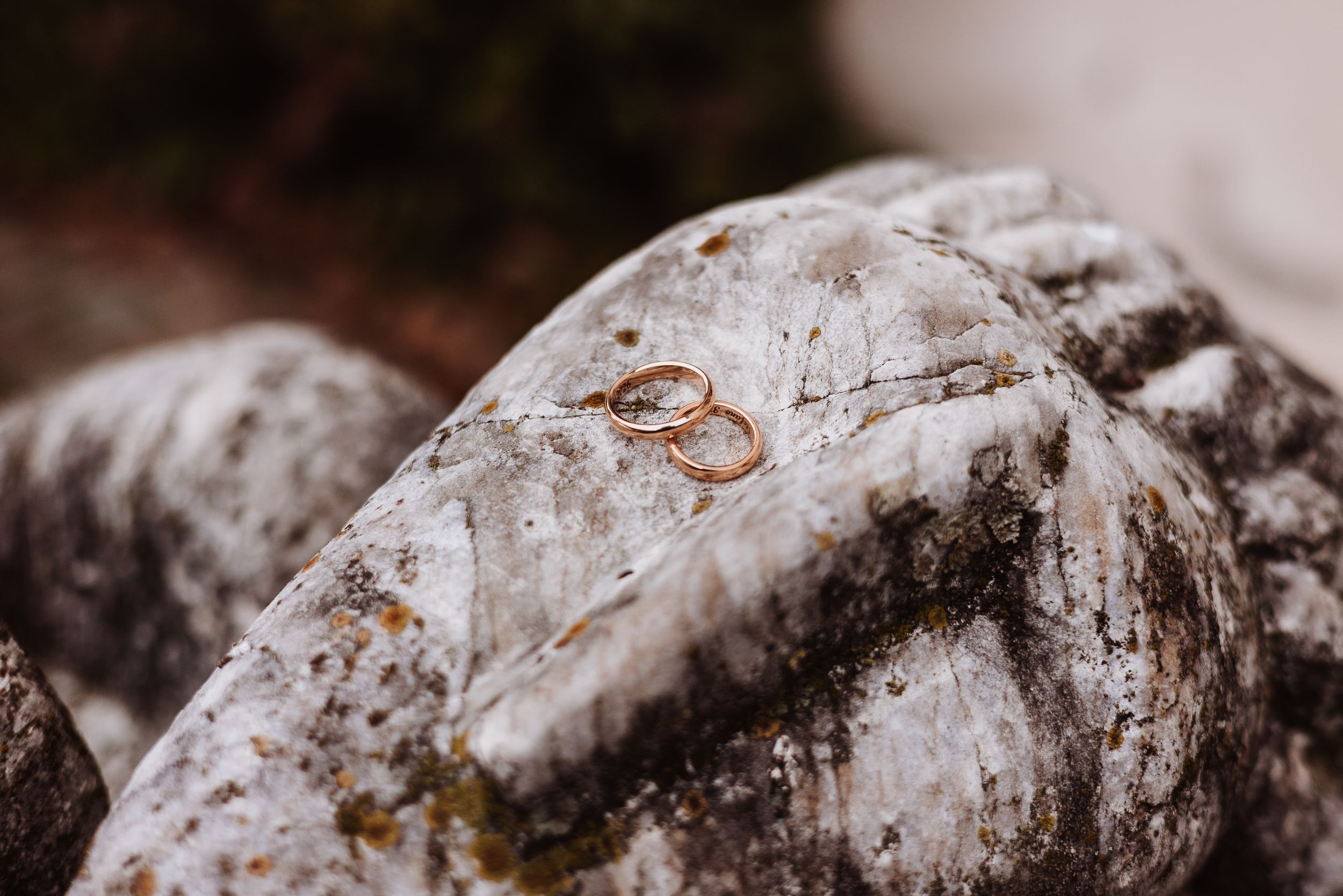 Two gold wedding rings resting on a textured gray rock surface outdoors.