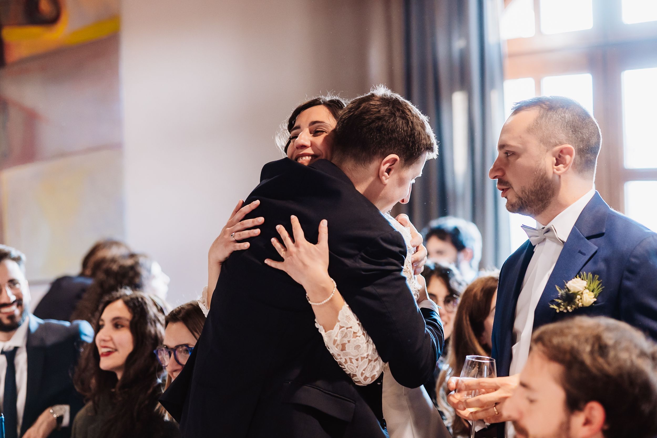 Guests sharing warm hugs and smiles at an elegant indoor wedding reception celebration.