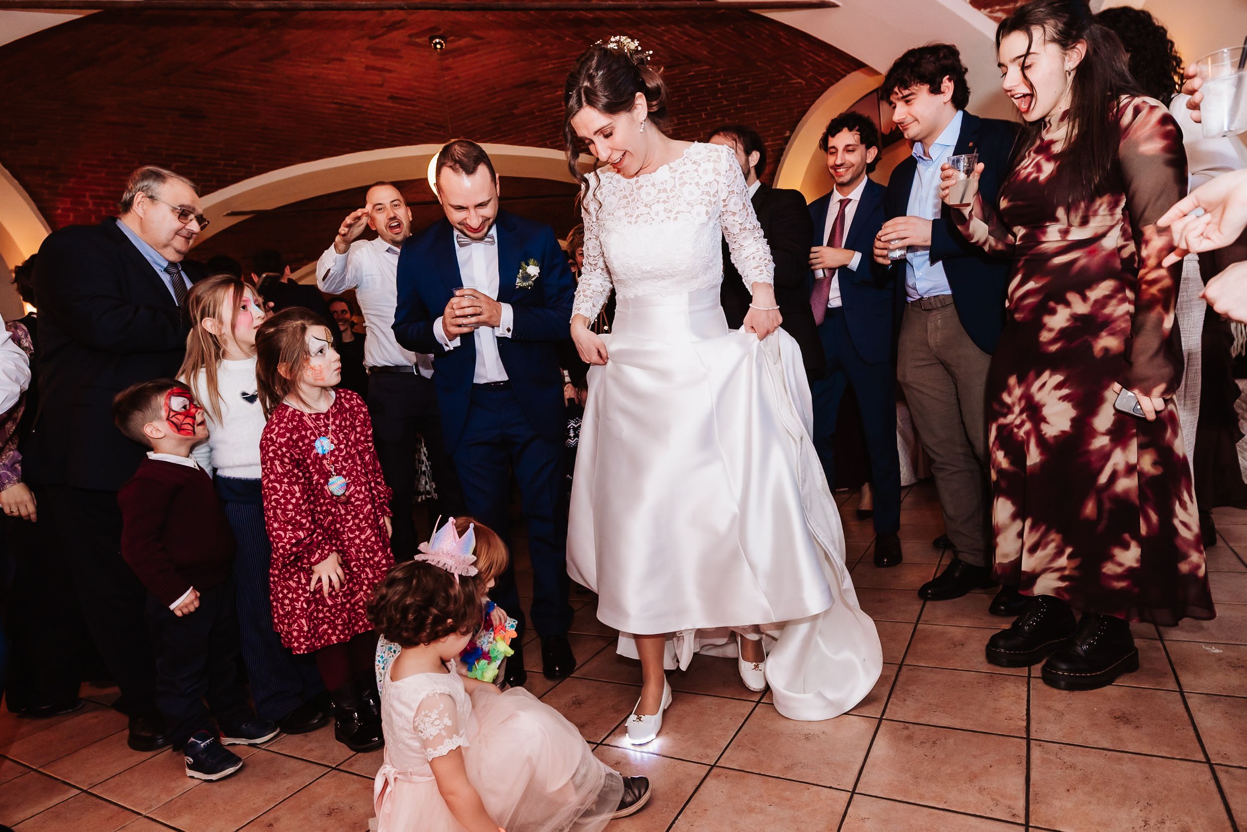 Bride and groom dancing joyfully with guests and children at a lively wedding reception celebration.