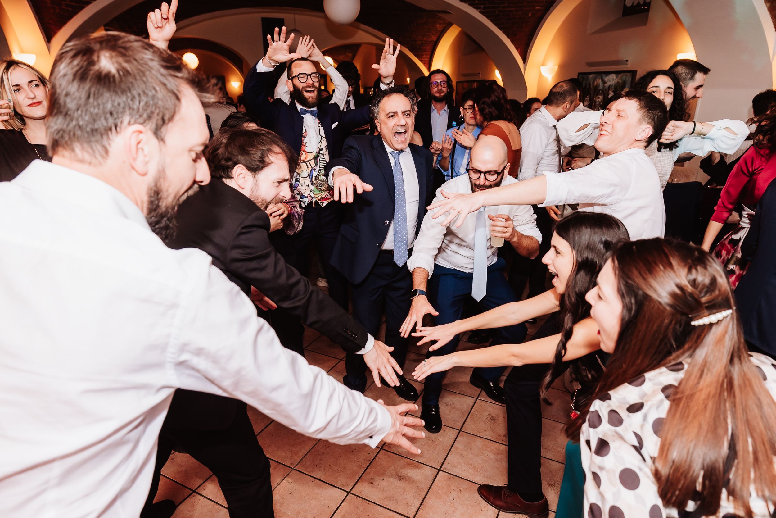 Lively wedding reception dance floor with guests celebrating, raising hands and dancing together in an elegant venue.