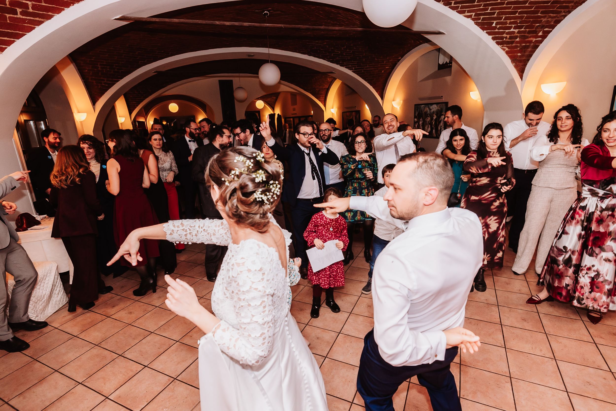 Bride and groom share first dance surrounded by guests at elegant wedding reception venue with arched ceilings.