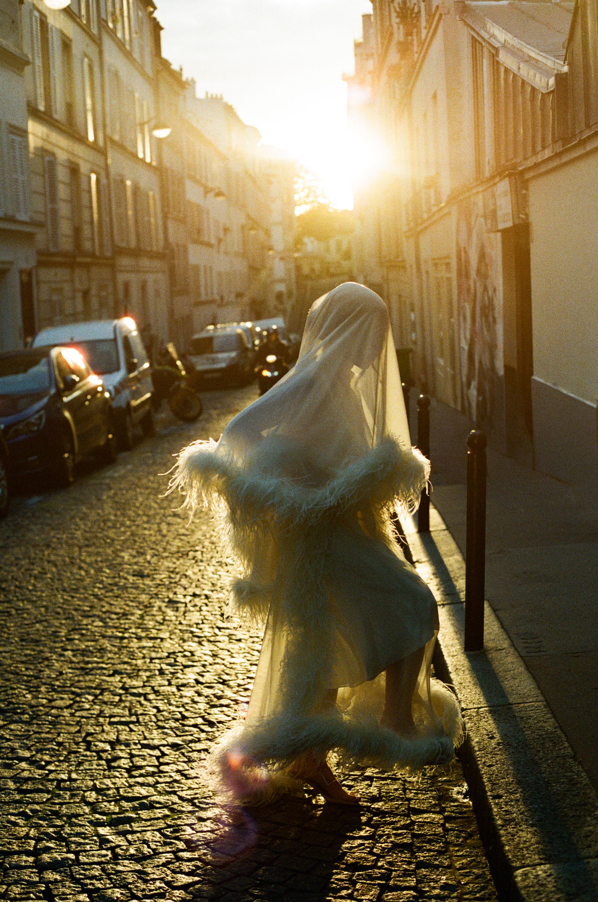Bride n a fluffy feather dress cobblestone streets bathed in golden sunset light in Paris. Montmartre fashion wedding photos. film