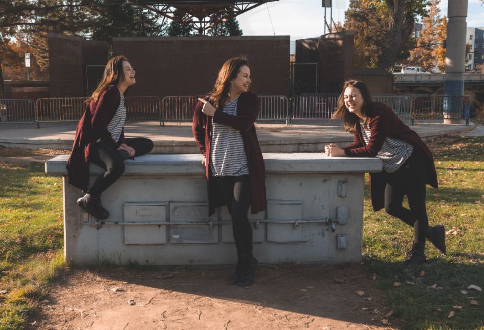 3 images combined of same young woman to appear she laughing and socializing with herself outdoors near a concrete wall on a sunny day.