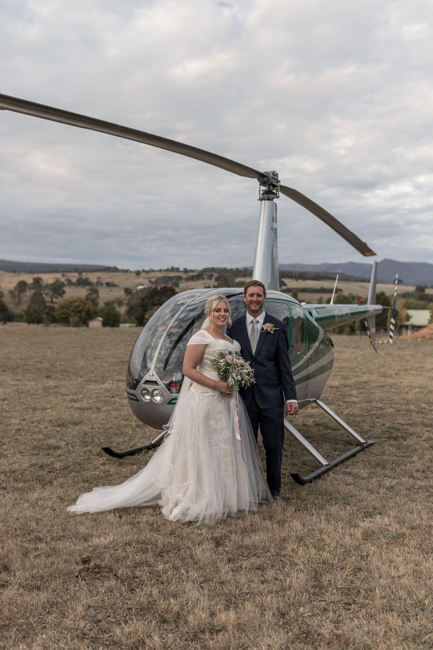 Bride and groom posing in front of a helicopter on a rural field on their wedding day.