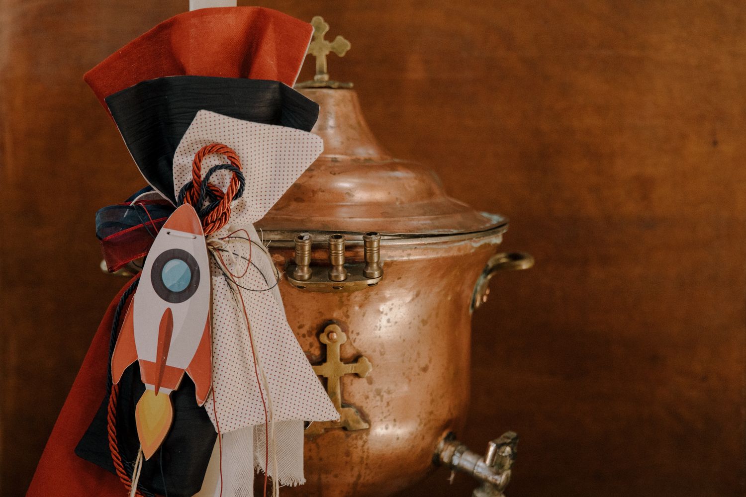 Copper samovar decorated with colorful ribbons and a rocket motif against a warm brown background.