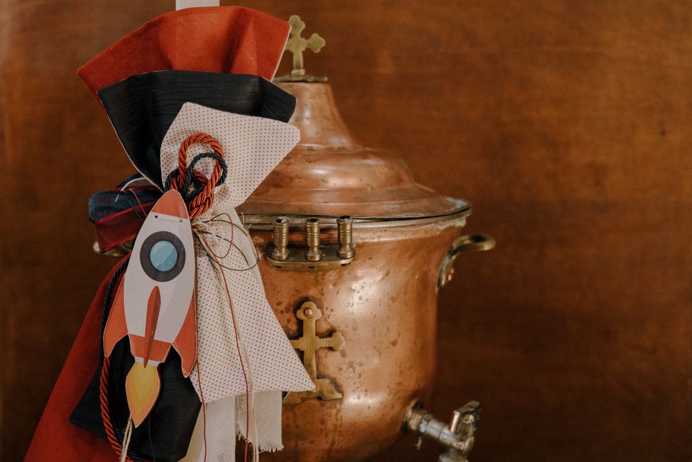 Copper samovar decorated with colorful ribbons and a rocket motif against a warm brown background.