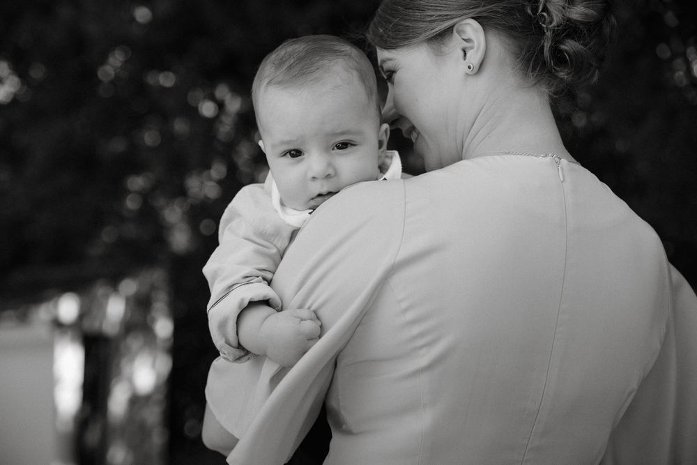 Black and white photo of a mother tenderly holding her baby, with trees softly blurred in the background.