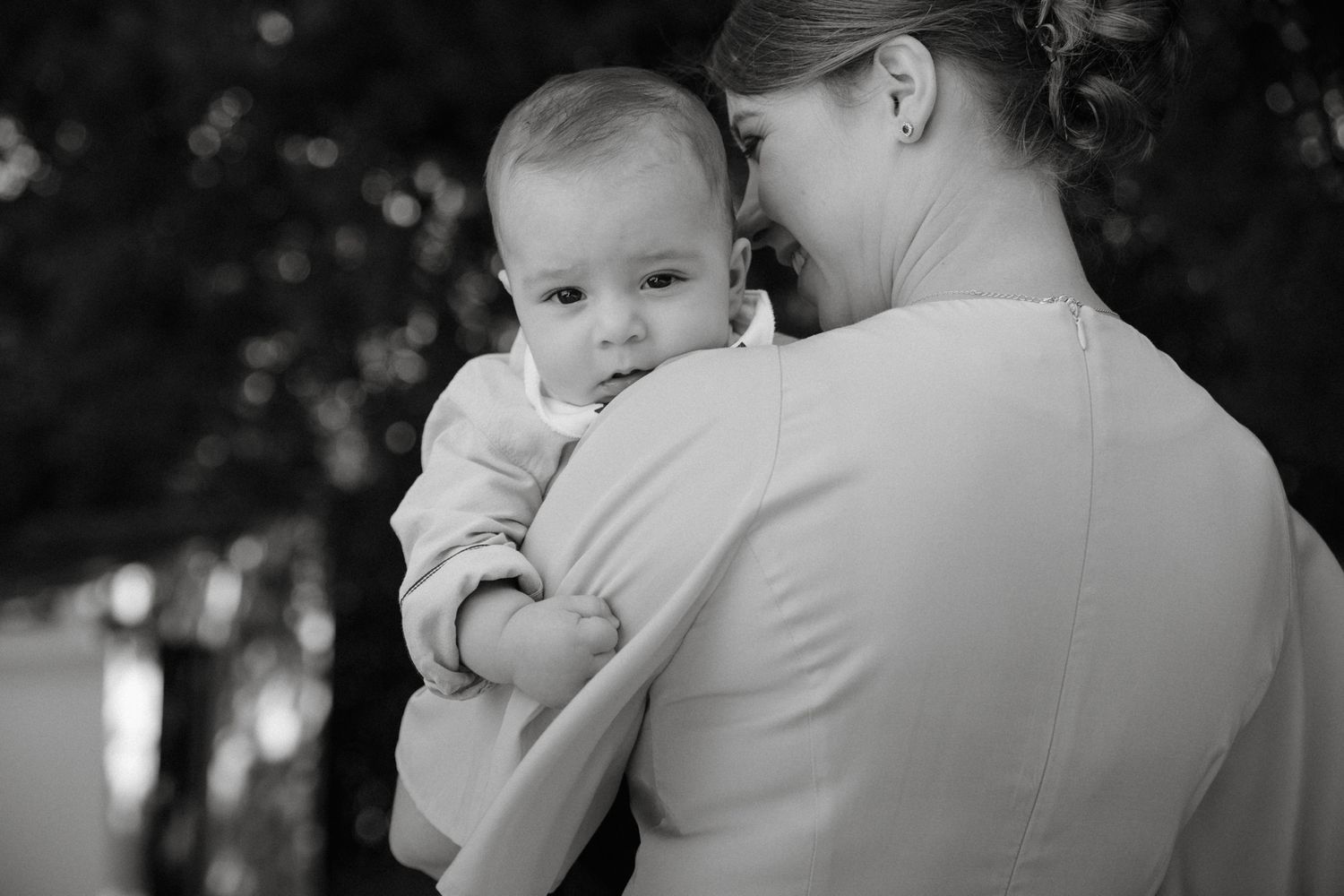 Black and white photo of a mother tenderly holding her baby, with trees softly blurred in the background.