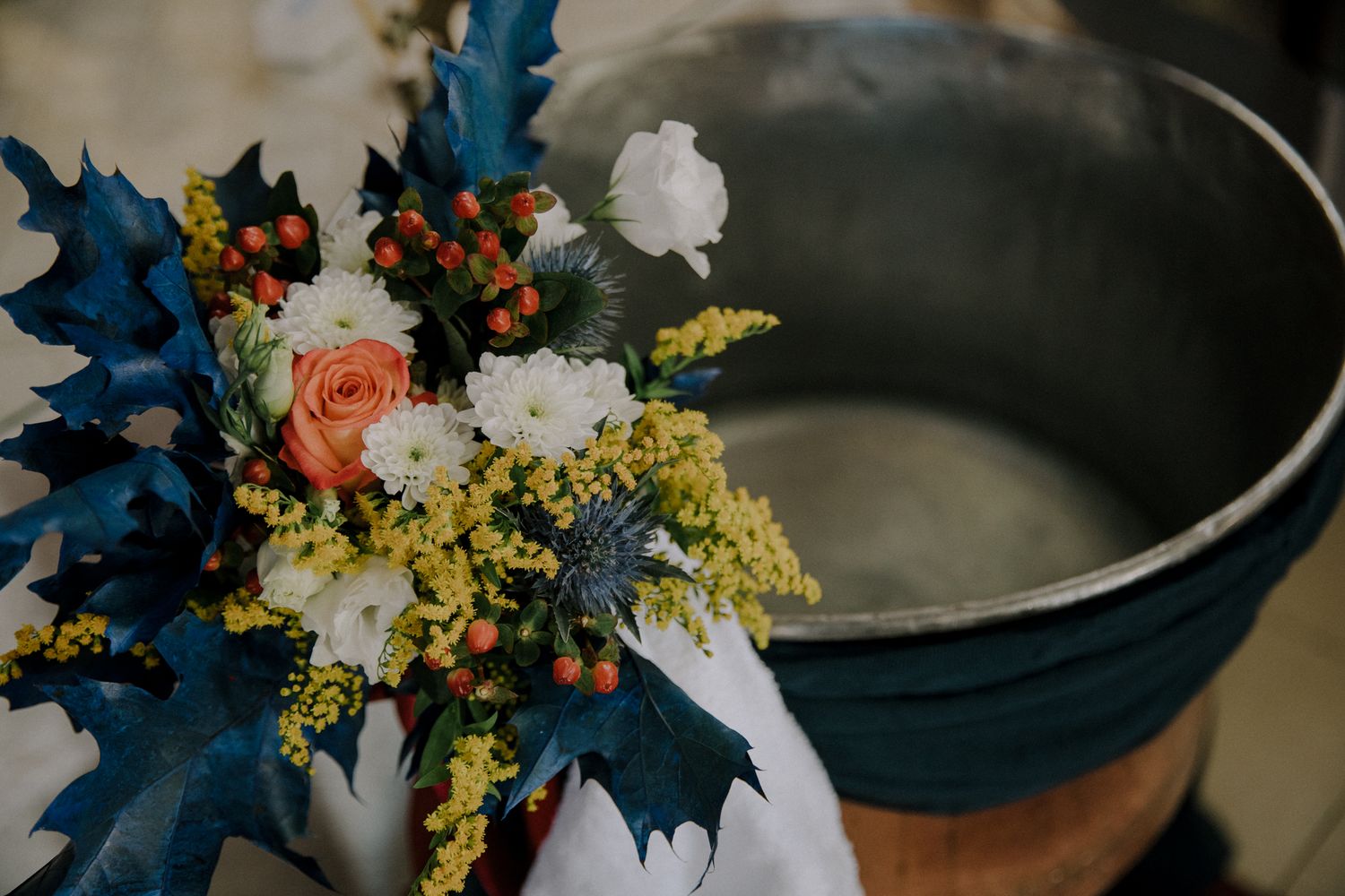 Colorful christening floral arrangement with pink roses, white blooms, yellow flowers, and blue thistles beside a silver basin.