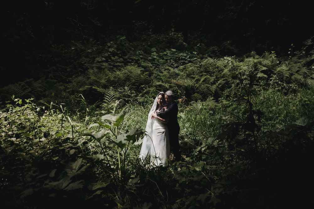 A bride and groom embrace romantically in a lush green forest setting during their outdoor wedding ceremony.