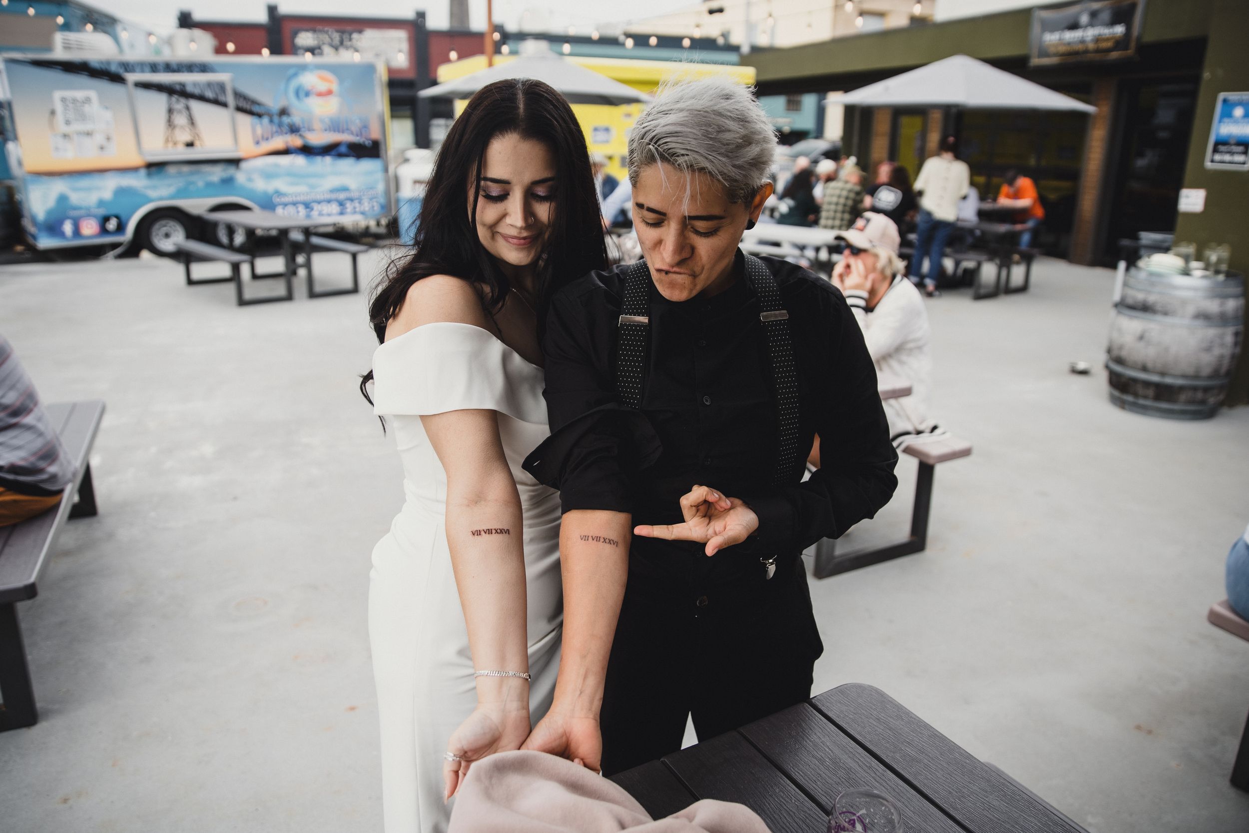 Couple examining a tattoo on a womans forearm at an outdoor venue during a casual event.