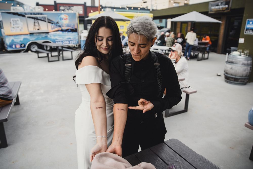 Couple examining a tattoo on a womans forearm at an outdoor venue during a casual event.