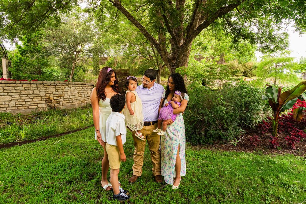 Family of five sharing a joyful moment outdoors under lush green trees in a garden setting.