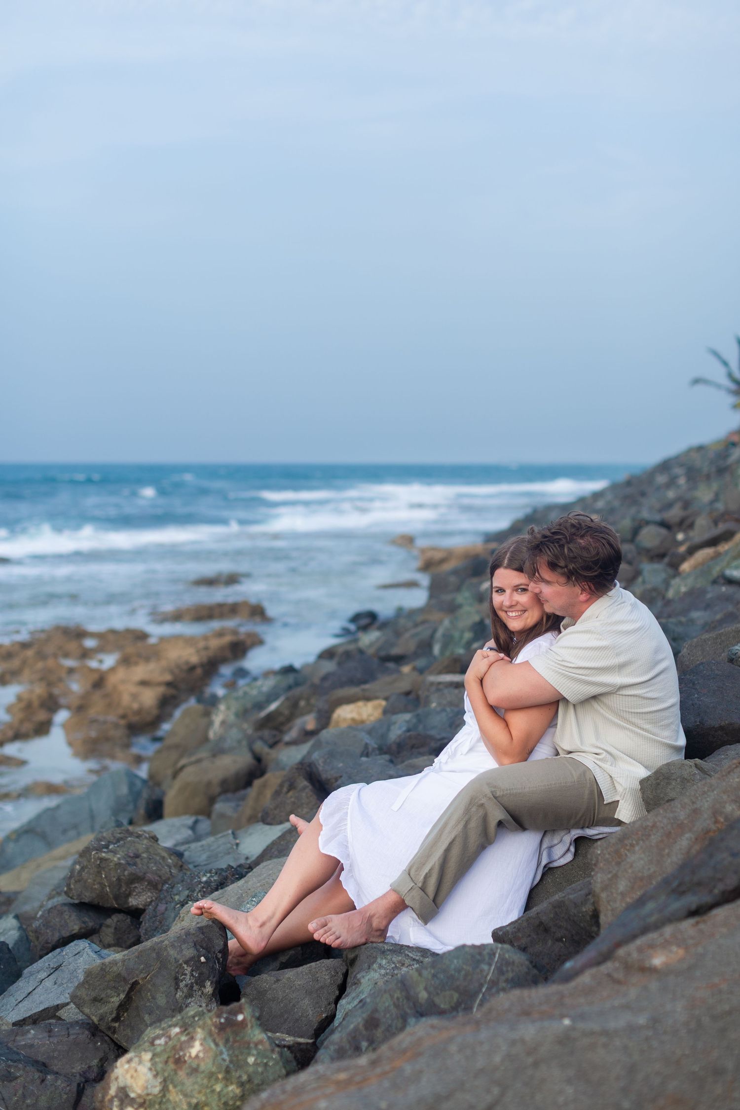 Couples portrait seated on the rocks at Balneario del Escambrón in Old San Juan, Puerto Rico.
