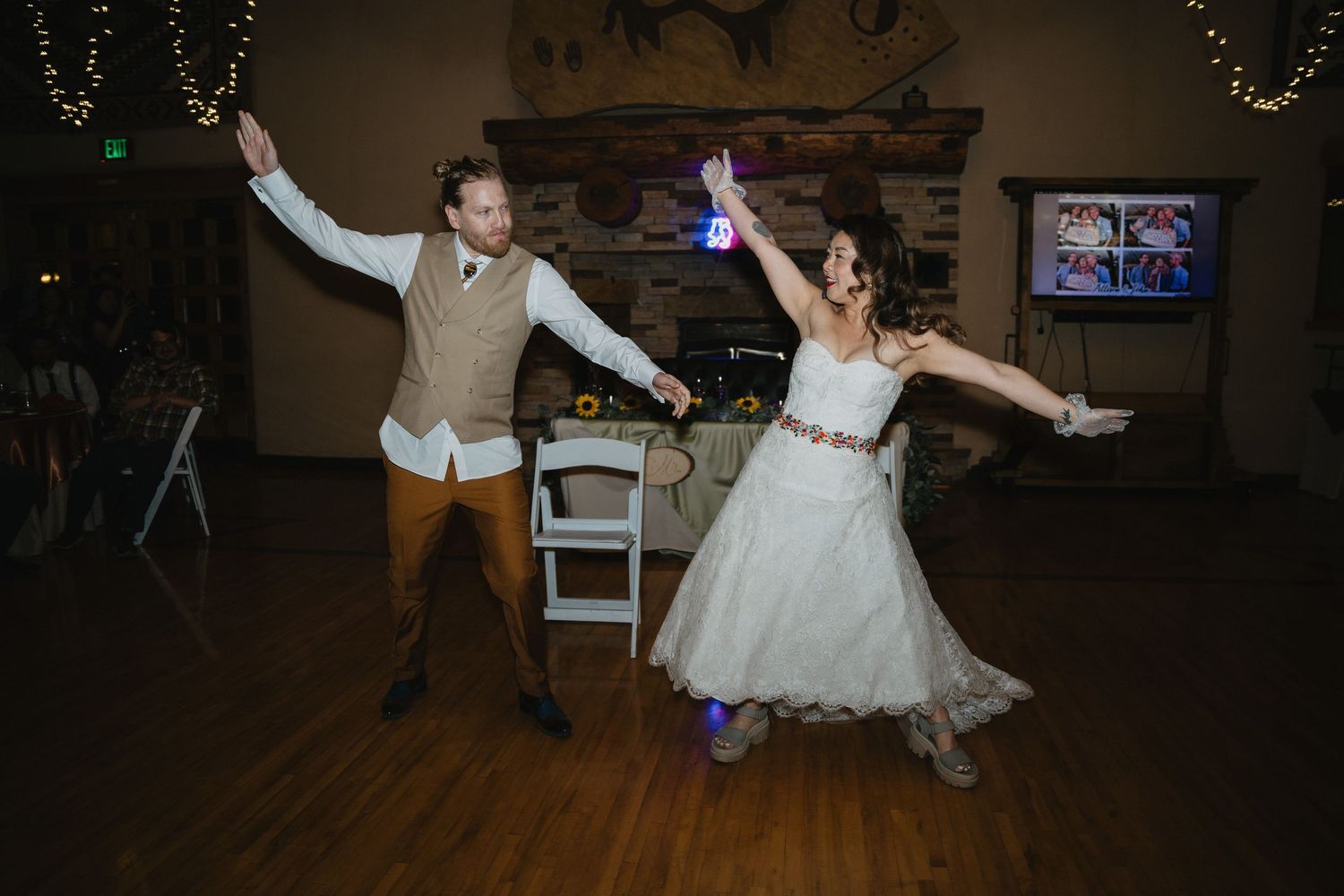 Bride and groom celebrate with outstretched arms during energetic first dance at rustic wedding reception.