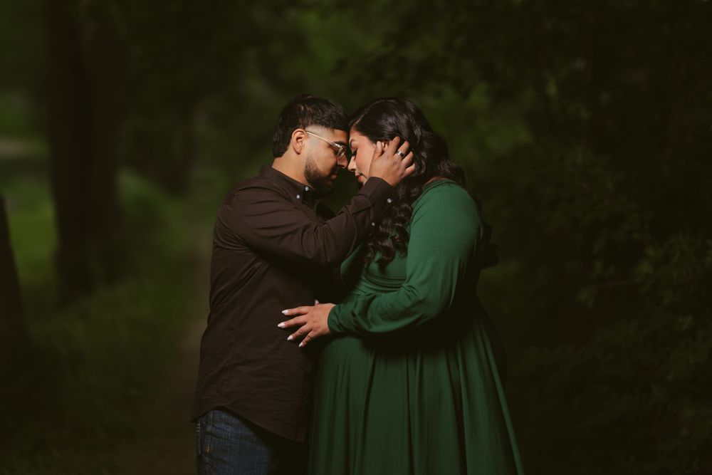 Romantic couple sharing an intimate forehead touch moment in a lush green forest, woman in emerald dress.
