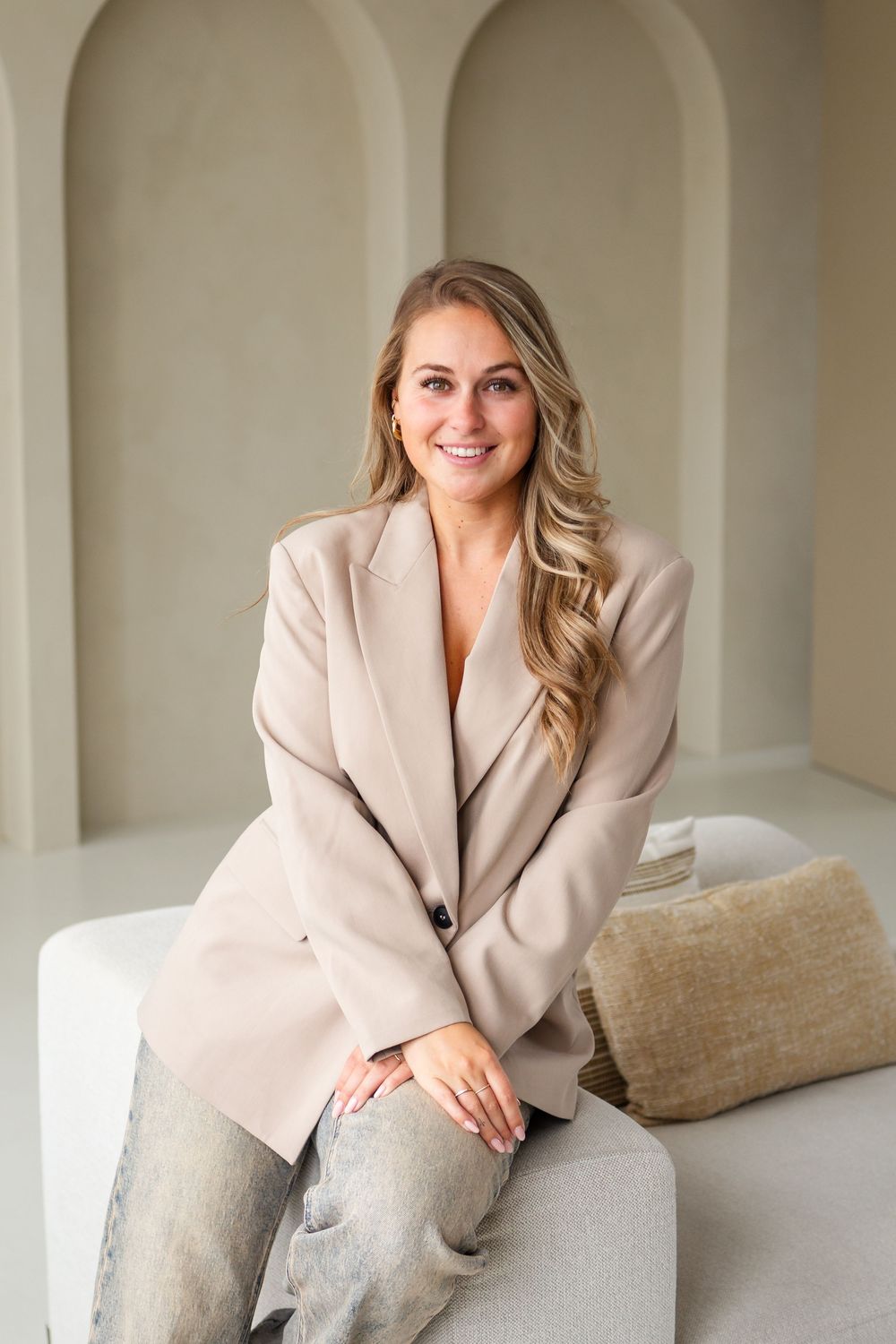 Fashion portrait series showcasing a beige blazer styled with neutral decor against arched wall architecture.