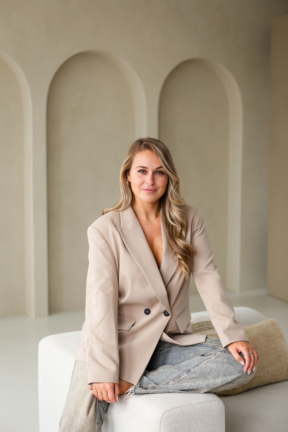 Professional portrait series showing someone in a beige blazer posing against an elegant arched wall background.
