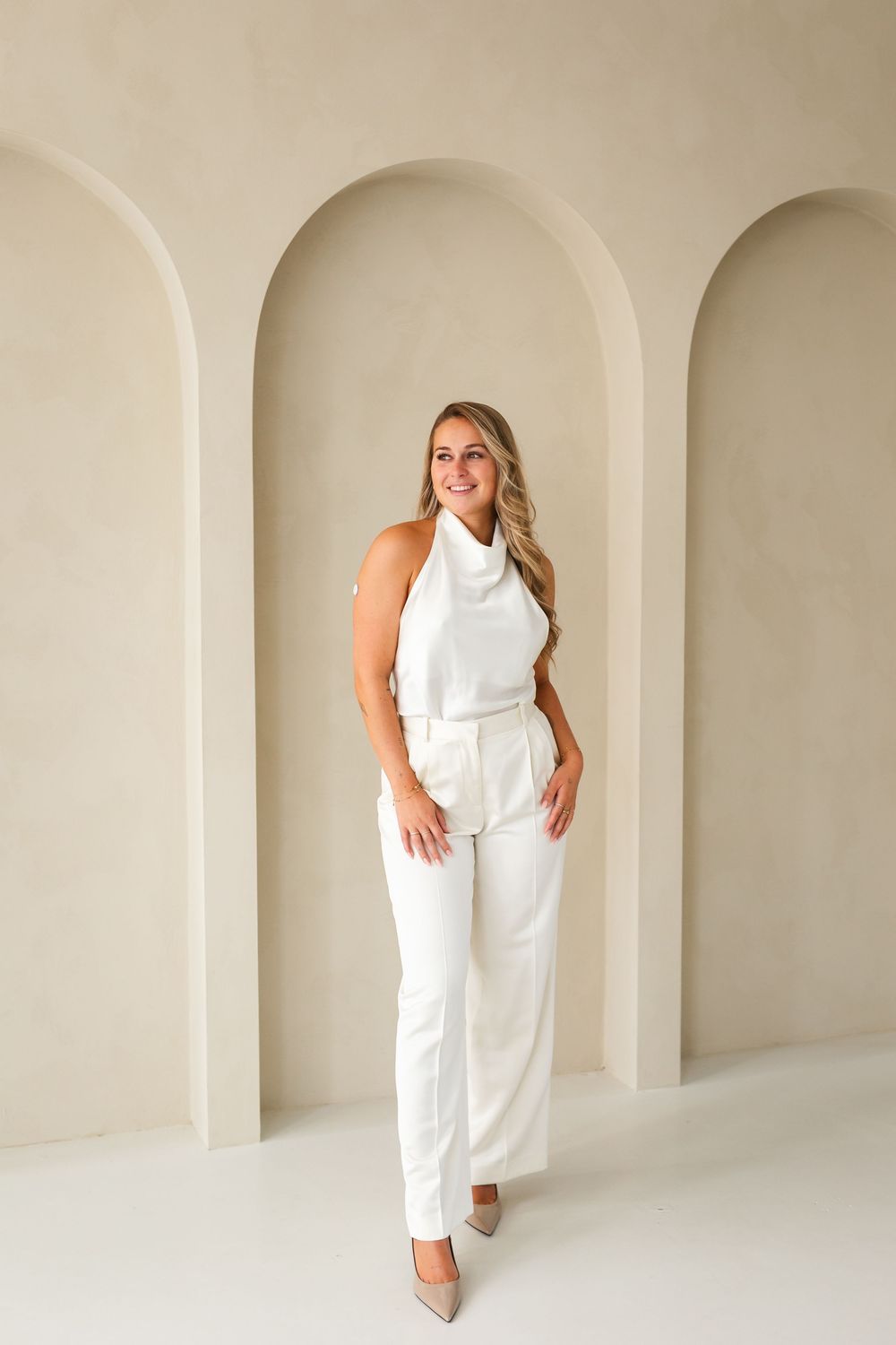 Professional fashion photography series featuring an all-white pantsuit outfit against a minimalist arched backdrop.