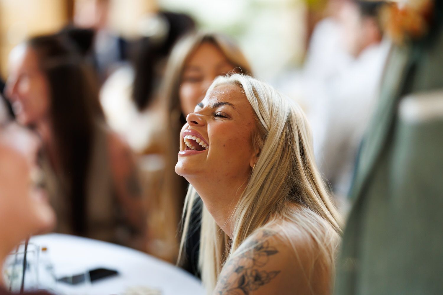 Blonde woman with tattoos laughing joyfully at a social gathering event.