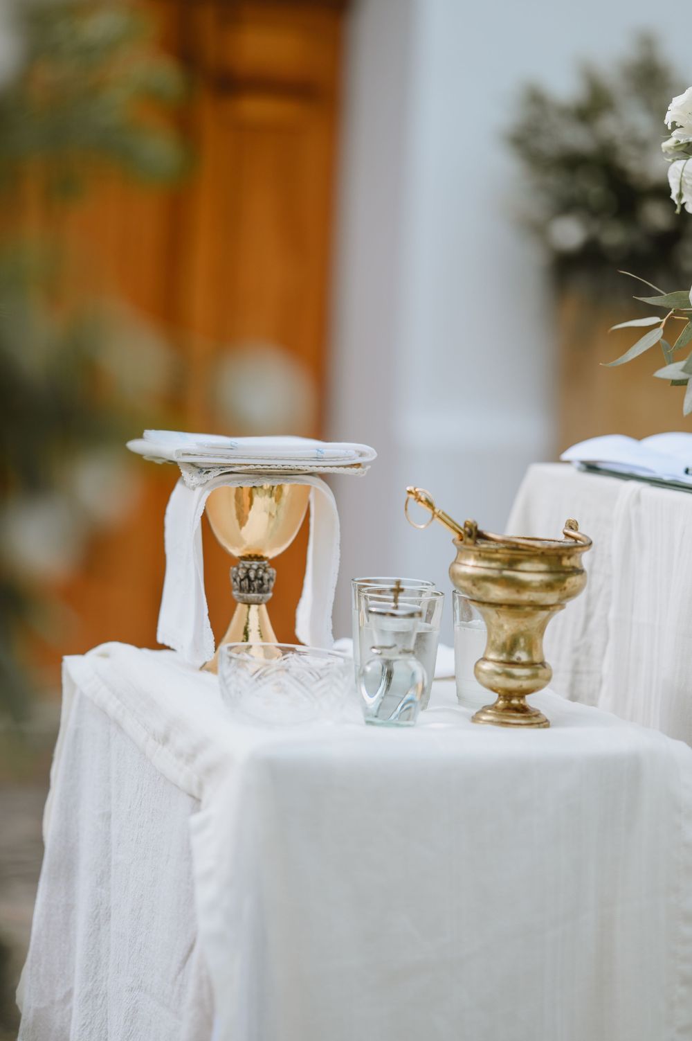 White linen altar table with gold chalice, aspergillum, and candle set up for a Catholic wedding ceremony.