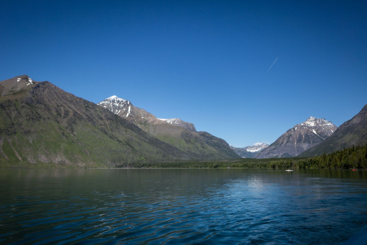 Yellow canoe on the shore of a calm mountain lake with a wooden dock and snow-capped peaks under blue sky.