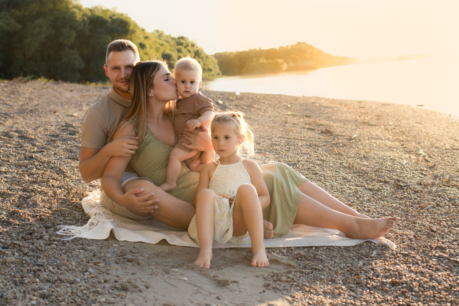 Family of four sitting on a sandy beach at golden hour, parents with two young children smiling warmly.