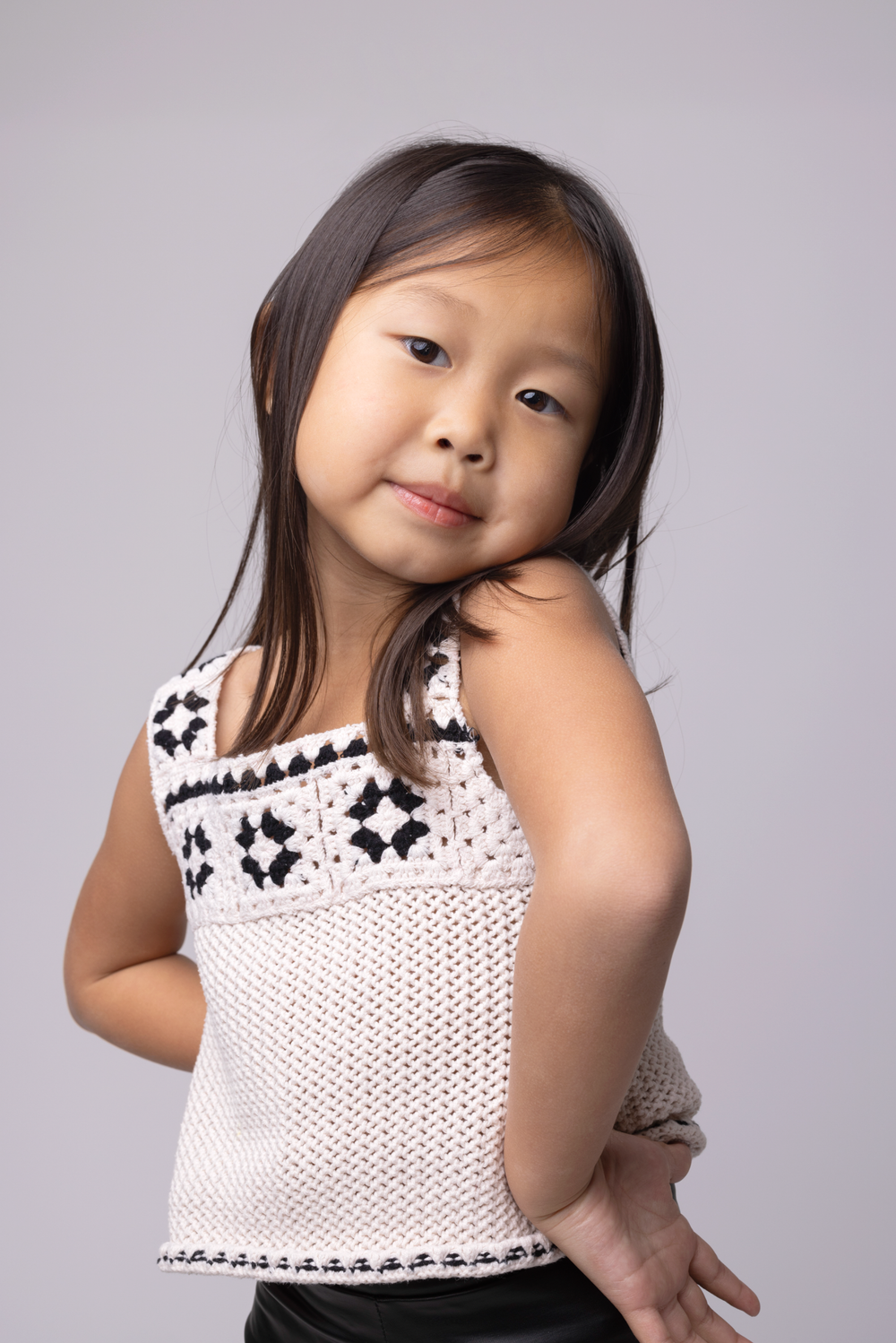 A young child in a white polka dot dress with black lace trim poses playfully in a photo series.
