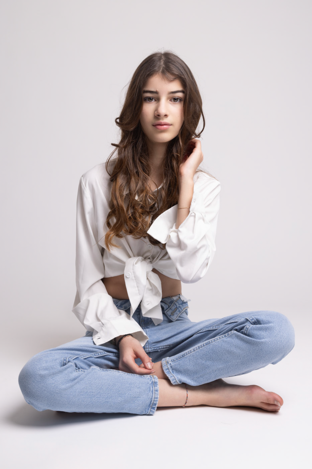 Model in white button-down shirt and blue jeans poses gracefully on white background in fashion photoshoot series.