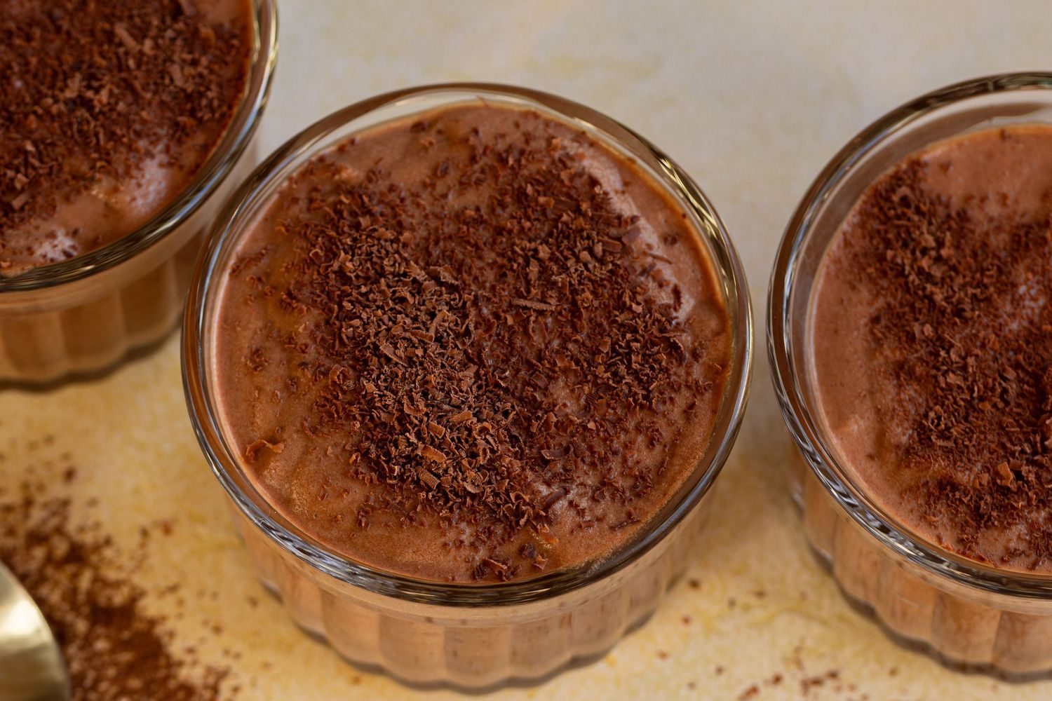 Chocolate mousse desserts in glass jars with dark chocolate chunks scattered on a light surface.