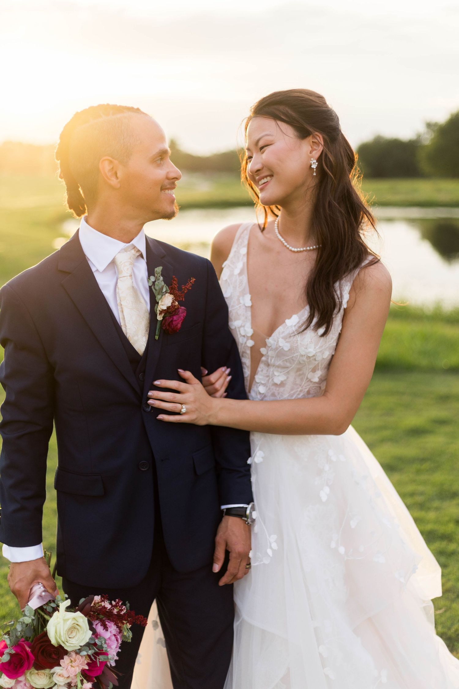 Bride and groom share a romantic moment outdoors at golden hour, with the bride in a white gown and groom in a navy suit.