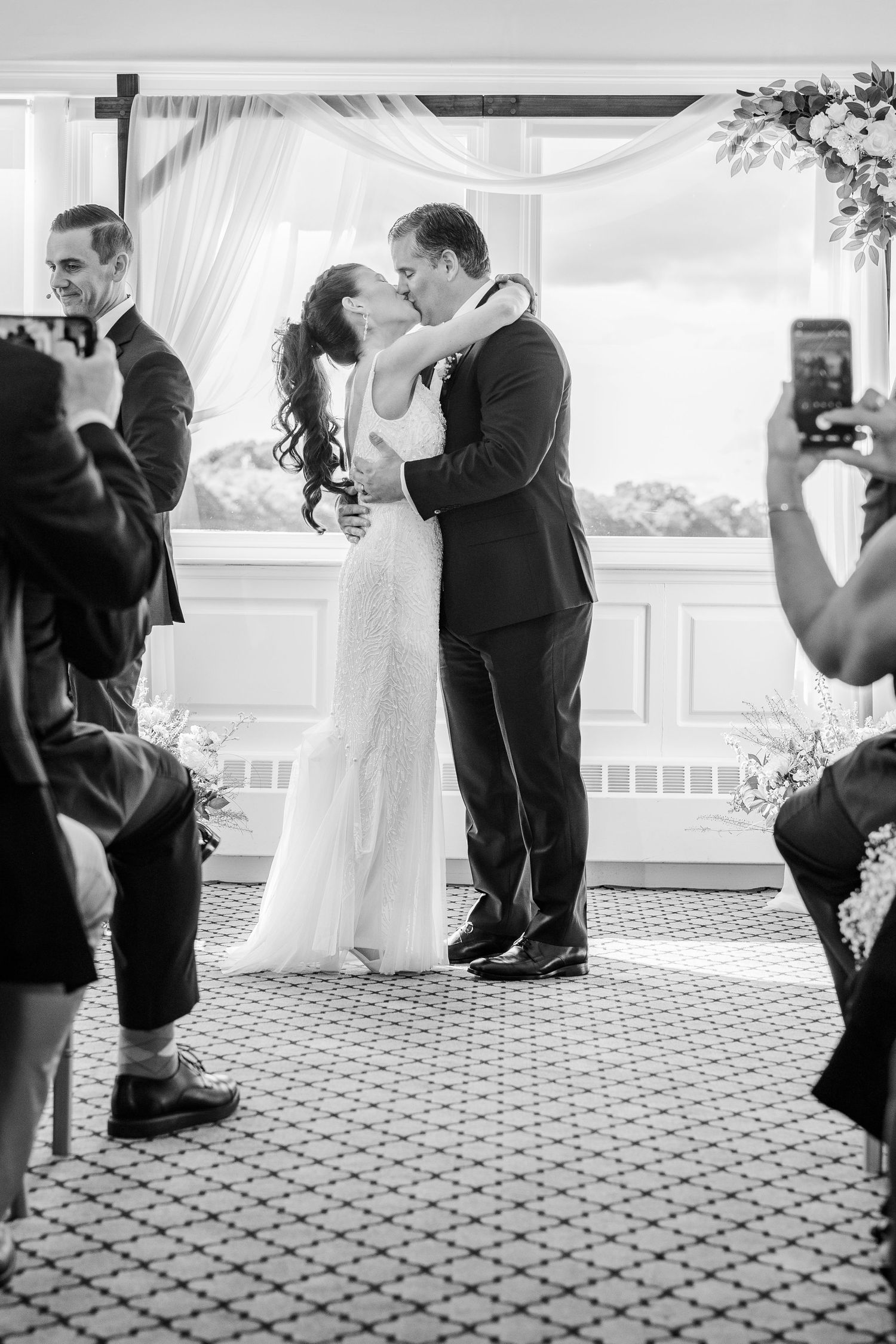 Black and white photo of a bride and groom sharing their first kiss at the wedding altar.