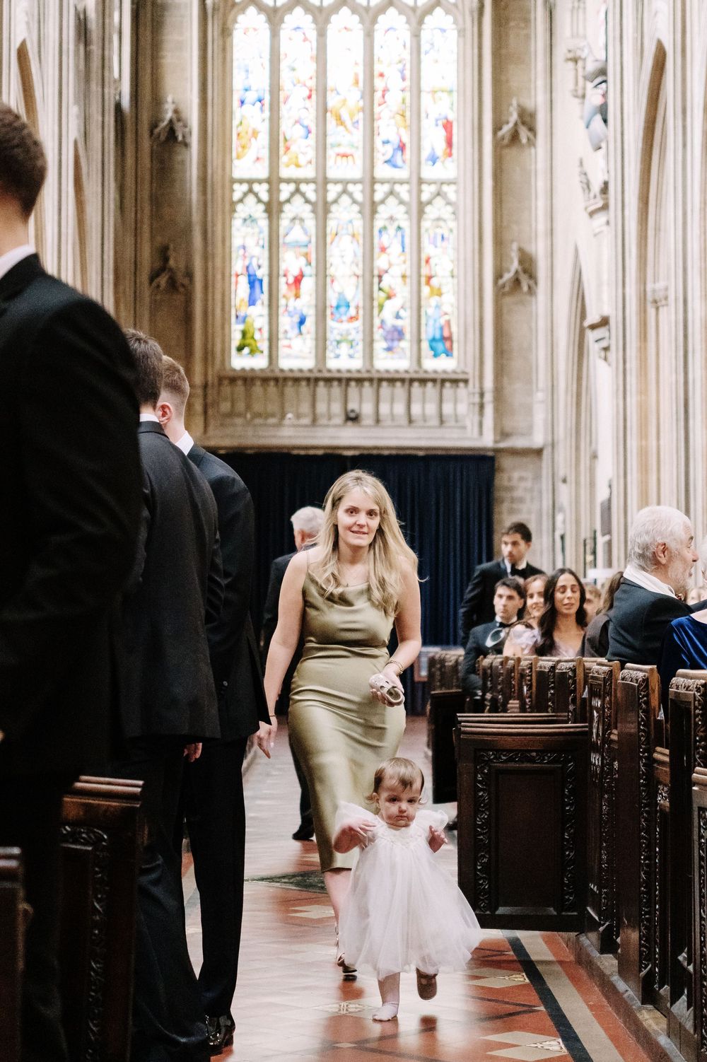 A bridesmaid in a sage green dress walks a flower girl in white down the aisle of St Mary Redcliffe Church, Bristol Wedding