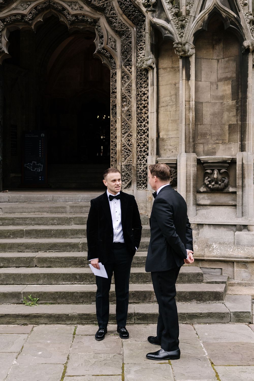 Groom in formal black suits converse outside St Mary Redcliffe Church, Bristol Wedding