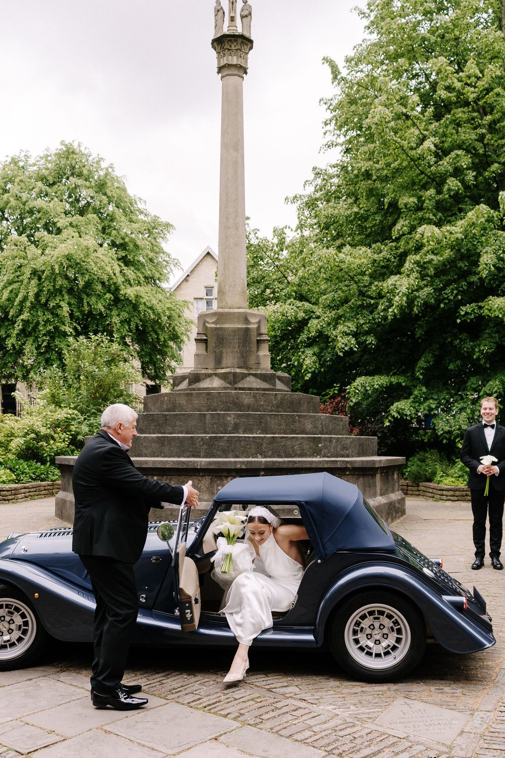 Bride stepping out of a vintage navy blue convertible car assisted by St Mary Redcliffe Church, Bristol Wedding
