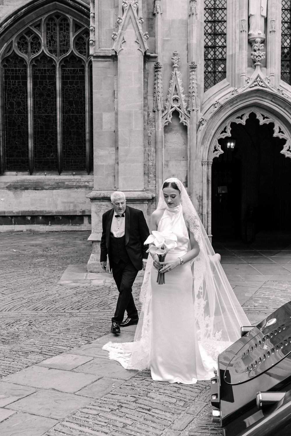 Black and white photo of a bride in a long veil holding bouquet walking St Mary Redcliffe Church, Bristol Wedding
